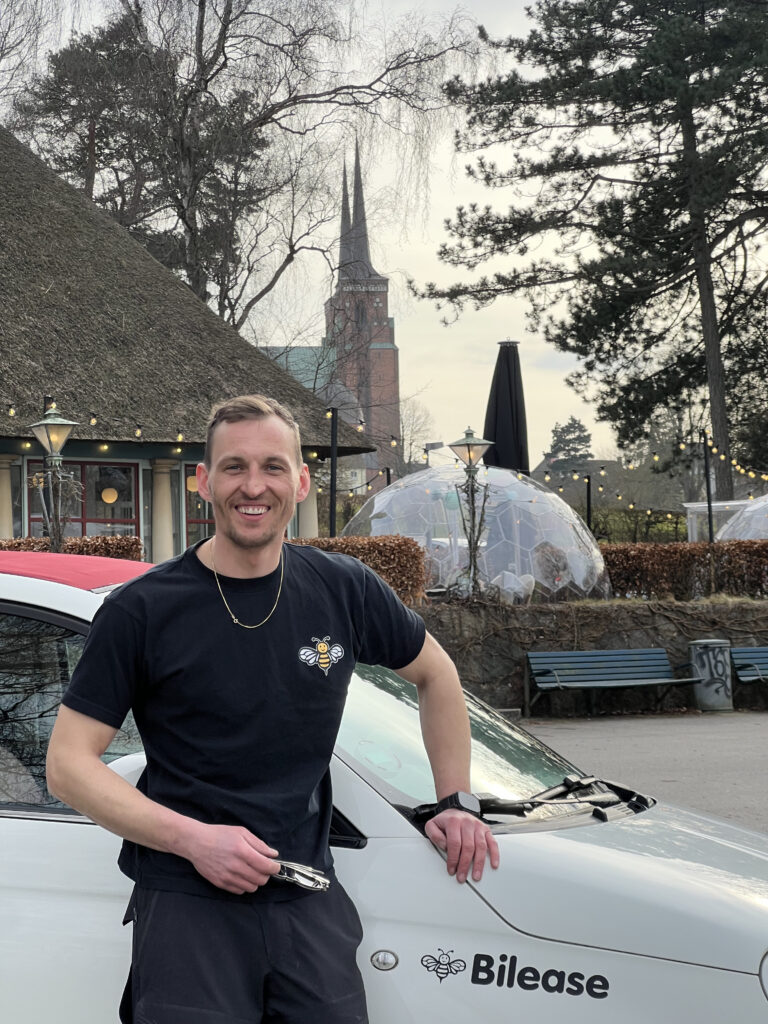 Glad medarbejder fra Bilease, står foran en Fiat 500c med rødt tag. I baggrunden kan man se pipers hus glas kuppler og roskilde domkirkes spir